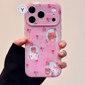 Pu&ograve; includere: Custodia per telefono rosa con finitura glitterata, con disegni di gatti e orsi dei cartoni animati e piccoli accenti floreali rossi. La custodia ha ritagli per la fotocamera e il flash. La custodia &egrave; tenuta da una persona.