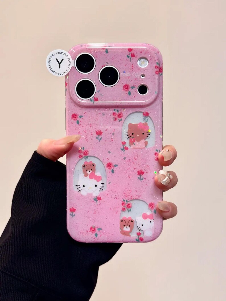 Pu&ograve; includere: Custodia per telefono rosa con finitura glitterata, con disegni di gatti e orsi dei cartoni animati e piccoli accenti floreali rossi. La custodia ha ritagli per la fotocamera e il flash. La custodia &egrave; tenuta da una persona.