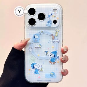 May include: Clear phone case with a blue and white checkered pattern, featuring Snoopy and other Peanuts characters. The case has a variety of stickers and the text "Happiness is a warm puppy."