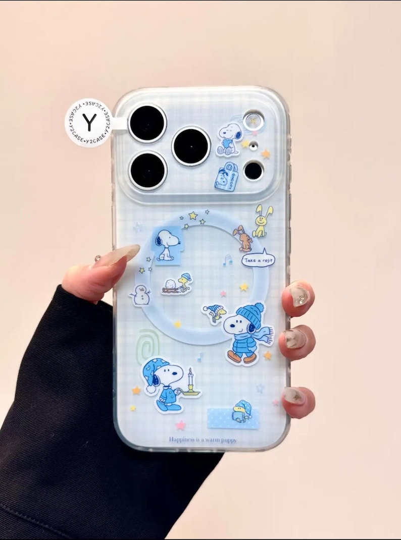 May include: Clear phone case with a blue and white checkered pattern, featuring Snoopy and other Peanuts characters. The case has a variety of stickers and the text "Happiness is a warm puppy."