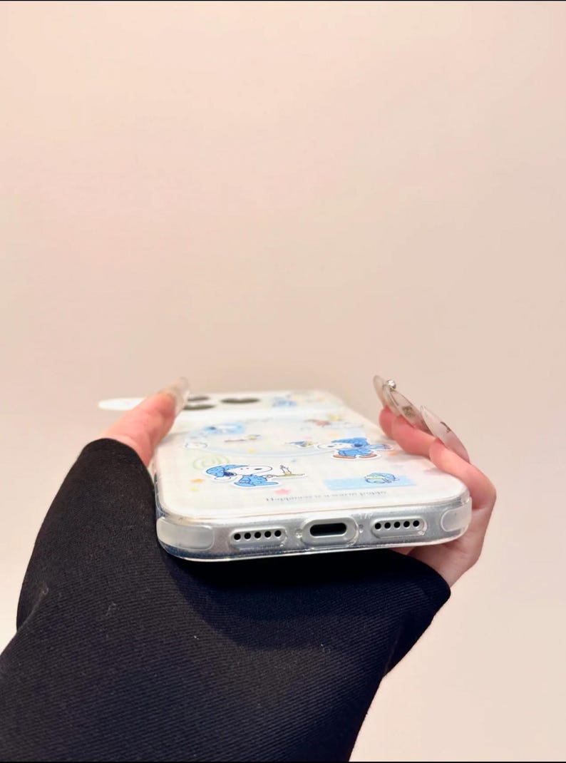 May include: Clear phone case with a cartoon character design in blue. The case has a transparent border and features a series of small holes and openings for the phone's features. The design includes various cartoon figures and shapes.