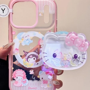 Könnte beinhalten: Rosa und transparente Handyhülle mit Sanrio-Charakteren. Die Hülle hat einen rosa Rand und eine transparente Rückseite mit Streifenmuster. Das Design umfasst Hello Kitty und andere Charaktere. Die Hülle hat einen schleifenförmigen Anhänger.