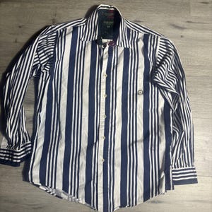 May include: A long-sleeved button-down shirt with vertical navy blue and white stripes. The shirt has a chest pocket and a collar. The cuffs and collar have a navy blue trim. The shirt is made of a lightweight fabric.