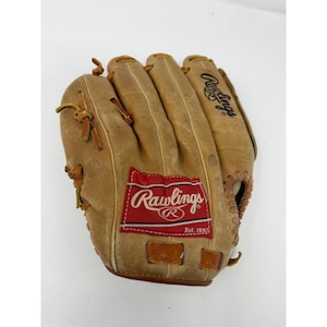 Puede incluir: Un guante de béisbol de cuero marrón claro, con el logotipo de Rawlings en rojo y blanco. El guante muestra signos de uso y costuras visibles. El logotipo de Rawlings está en un parche rectangular rojo. Diseñado para atrapar una pelota de béisbol.