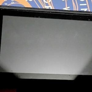 May include: A black handheld gaming console with a large screen. It has a blue controller on the left and a red controller on the right. The controllers have buttons and joysticks for gameplay. The screen is blank.