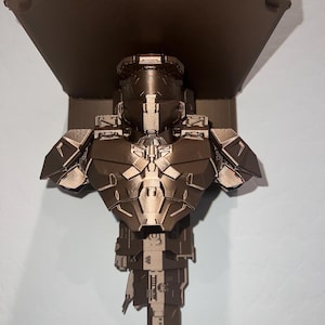 Puede incluir: Una estantería de pared de color bronce con un busto detallado de un soldado espartano de la serie de videojuegos Halo. La estantería incluye el logotipo de Halo y está montada en una pared azul claro.