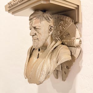 May include: A beige 3D-printed wall shelf featuring a bust of Obi-Wan Kenobi from Star Wars. The shelf includes the Star Wars logo and a Millennium Falcon design. The bust is detailed with facial features and clothing.