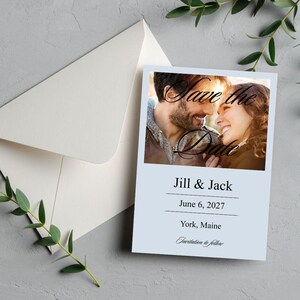 Puede incluir: Una tarjeta de invitación de boda azul claro con una foto de una pareja sonriente. La tarjeta dice "Save the Date", seguida de "Jill & Jack", la fecha y el lugar. Un sobre y vegetación están en el fondo.