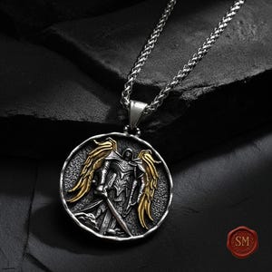St michael pendant isolated on black background, bold christian necklace with armor of god symbolism, oxidized silver tone and antique gold wing detail.