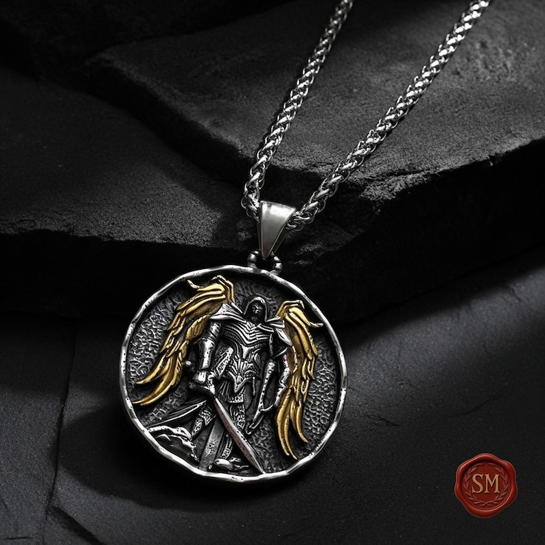 St michael pendant isolated on black background, bold christian necklace with armor of god symbolism, oxidized silver tone and antique gold wing detail.
