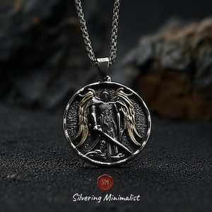Detailed st michael pendant with gold plated wings and oxidized antique silver finish resting on dark stone surface, bold christian necklace inspired by the armor of god symbolism.
