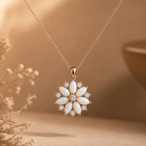 May include: A rose gold necklace featuring a flower-shaped pendant. The pendant is composed of marquise-cut white opals arranged as petals, with small round clear stones set between them and a single clear stone at the center of the flower.