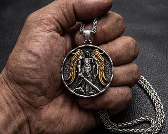 May include: A silver-toned pendant necklace featuring a detailed warrior figure with golden wings and a sword. The round pendant is suspended from a silver chain. The design has a vintage, antique look.