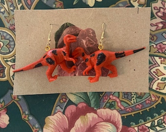Könnte beinhalten: Ein Paar rote und schwarze Dinosaurier-Ohrringe mit goldenen Haken. Die Dinosaurier schauen sich an und haben schwarze Flecken.