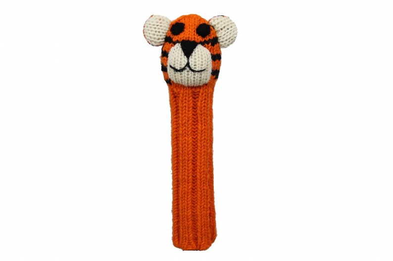 May include: Orange and black knitted golf club head cover with a tiger face. The tiger has white ears, a white nose, and black eyes.