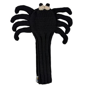 May include: A black knitted golf club headcover shaped like a spider with eight legs extending from the sides. The headcover features two small, round, cream-colored eyes at the top and a long, ribbed, tubular body designed to fit over a golf club shaft.