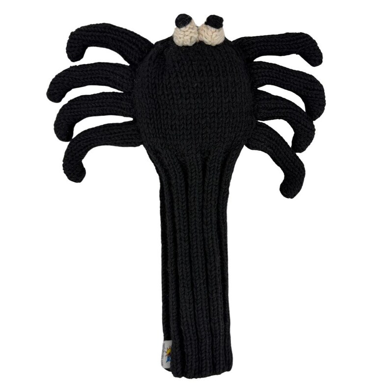 May include: A black knitted golf club headcover shaped like a spider with eight legs extending from the sides. The headcover features two small, round, cream-colored eyes at the top and a long, ribbed, tubular body designed to fit over a golf club shaft.