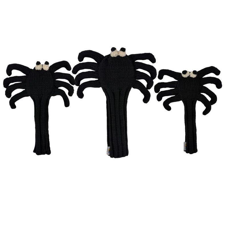 May include: Three black knitted spider-shaped golf club head covers. Each cover features a round body with eight extended legs and two small, cream-colored circular eyes positioned at the top. The covers have a long, ribbed neck section.