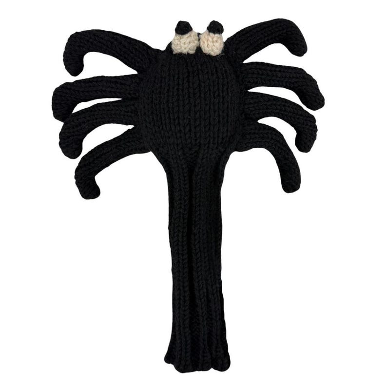 May include: A black knitted spider-shaped golf club headcover featuring eight long, flexible legs extending from a central body. The spider has two small, round, cream-colored eyes positioned at the top of the head, all crafted from yarn.