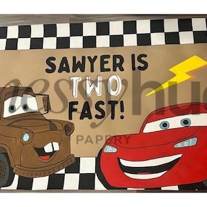 May include: A banner featuring the text "SAWYER IS TWO FAST!" with illustrations of Mater and Lightning McQueen from the Cars movie. The banner has a brown background and a black and white checkered border.