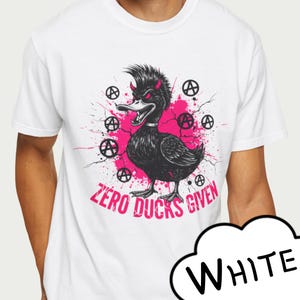 May include: White t-shirt featuring a black and white illustration of a punk duck with devil horns and the text "ZERO DUCKS GIVEN" in pink. The design includes anarchy symbols and pink paint splatters.