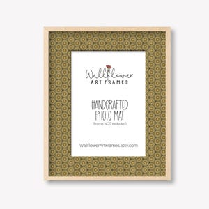 May include: A rectangular photo frame with a light wood finish. The frame features a patterned mat with a repeating floral design in shades of gold and brown. The text "Wallflower Art Frames" and "Handcrafted Photo Mat" are visible.