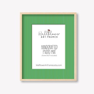 May include: A rectangular, light-colored wooden picture frame with a green and white striped mat. The frame holds a white mat with the text "Wallflower ART FRAMES" and "HANDCRAFTED PHOTO MAT" in black. The Etsy shop URL is also visible.