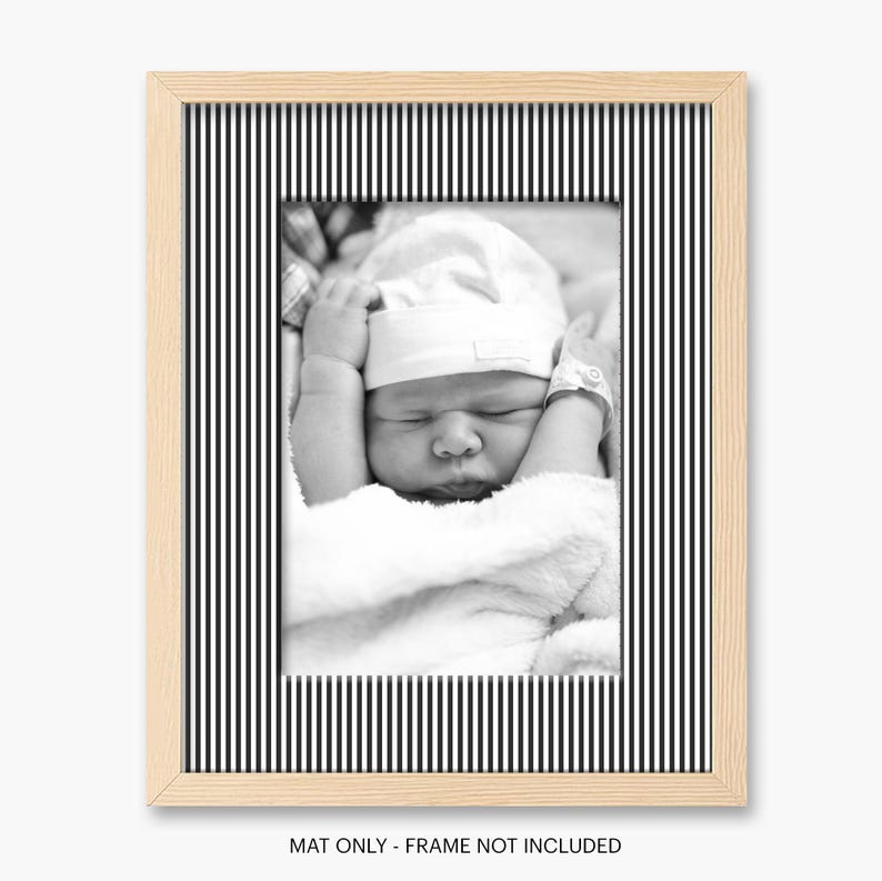 May include: A black and white photograph of a newborn baby in a white hat and blanket, framed in a light wood frame with a black and white striped border. The text at the bottom reads "MAT ONLY - FRAME NOT INCLUDED."