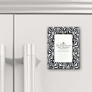May include: A small, rectangular picture frame with a black and white floral pattern. The frame is attached to a white surface. The frame has the text "Wallflower ART FRAMES handmade just for you WallflowerArtFrames.etsy.com".