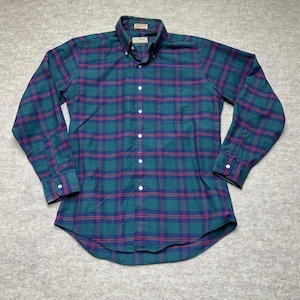 May include: Green, blue, and red plaid button-down shirt. The long-sleeved shirt has a button-down collar, a chest pocket, and white buttons. The shirt is made of a woven fabric.