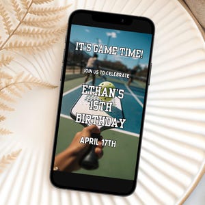 以下が含まれることがあります： スマートフォンには、ピックルボールをテーマにした誕生日の招待状が表示されています。「It's Game Time!」と書かれており、イーサンの15歳の誕生日が4月17日であることを発表しています。ピックルボールのパドルとボールが特徴です。