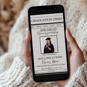 May include: A smartphone displays a graduation announcement. The headline reads "GRADUATION TIMES" with the text "SHE DID IT! Olivia is graduating." The announcement includes a photo of the graduate, date, time, and location. The phone is held by a person.