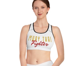 May include: White sports bra with black trim and the words "MUAY THAI Fighter" in gold and red lettering. The bra has a racerback design and is made of a smooth, athletic fabric. Ideal for martial arts training and fitness activities.