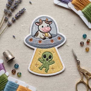 May include: Embroidered patch featuring a cow in a UFO, with an alien below. The cow is brown and white, wearing a bell. The UFO is gray with orange lights. The alien is green with outstretched arms, on a yellow background.