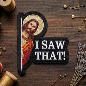May include: Embroidered patch featuring an image of Jesus with a halo, peeking out from behind a letter "P". The patch has the text "I SAW THAT!" in white on a black background. The patch is surrounded by sewing notions.