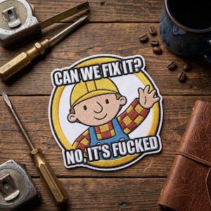 May include: Embroidered patch featuring a cartoon construction worker with the text "CAN WE FIX IT? NO, IT'S FUCKED" in a circular design. The patch is on a wooden surface with tools and a coffee cup.