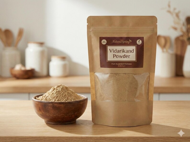 May include: A brown paper bag of Vidarikand Powder with a clear window, and a wooden bowl filled with the same powder. The bag has a brown label with white text. The background includes wooden kitchenware and white jars.