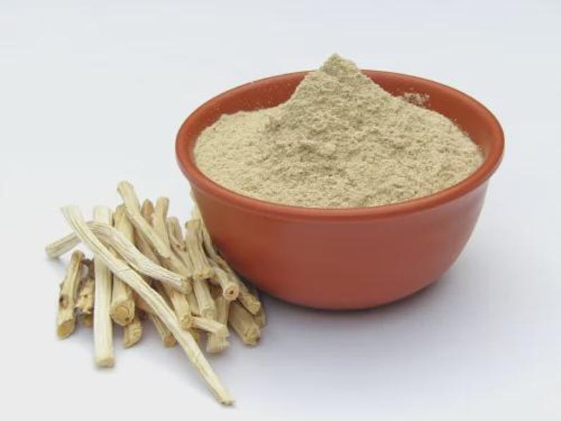 May include: A terracotta bowl filled with a light brown powder sits next to a pile of light-colored, dried sticks. The powder is finely ground, and the sticks have a rough texture. The items are set against a plain white background.