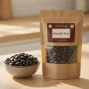 May include: A package of Kaunch Beej seeds with a clear window, next to a small bowl filled with similar seeds. The package has a brown label with the text "Nature Spring" and "Kaunch Beej". The seeds are dark brown.