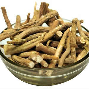 Op de afbeelding: Een heldere glazen kom gevuld met stukjes ashwagandha-wortel. De wortels zijn lichtbruin en beige van kleur, met een ruwe textuur. De kom staat tegen een witte achtergrond, waardoor de natuurlijke kleur en vorm van het kruidenproduct worden benadrukt.