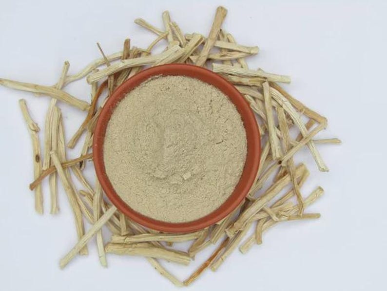 May include: Overhead shot of a small, round, terracotta-colored bowl filled with a fine, light beige powder. The bowl is surrounded by numerous pieces of dried, light-brown plant stems, all set against a white background.