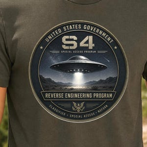 May include: An olive green t-shirt featuring a circular graphic with the text United States Government S4 Special Access Program and Reverse Engineering Program. The design depicts a metallic flying saucer hovering over a desert landscape at night.