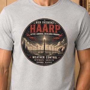 May include: A light gray t-shirt featuring a circular graphic with the text HIGH FREQUENCY HAARP ACTIVE AURORAL RESEARCH PROGRAM WEATHER CONTROL 62°23'30.6"N 145°9'2.1"W GAKONA, ALASKA. The illustration depicts a radio antenna array under a cloudy sky.