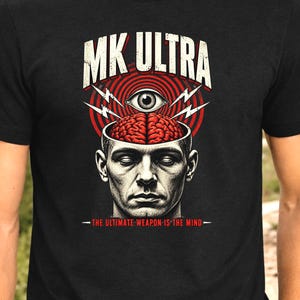 May include: A black t-shirt featuring a graphic print of a human head with the top removed to reveal a brain. Above the head is an eye surrounded by red concentric circles and lightning bolts. Text reads MK ULTRA and THE ULTIMATE WEAPON IS THE MIND.
