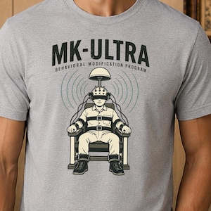 May include: A light gray t-shirt featuring a graphic of a person strapped to a chair with a device on their head, surrounded by concentric circles. The text "MK-ULTRA BEHAVIORAL MODIFICATION PROGRAM" is printed above the graphic.