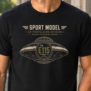 May include: Black t-shirt with a graphic design featuring the text "SPORT MODEL" and "S4 PROPULSION DIVISION". The design includes a stylized image of a UFO with the text "115 E115 ELEMENT 115".