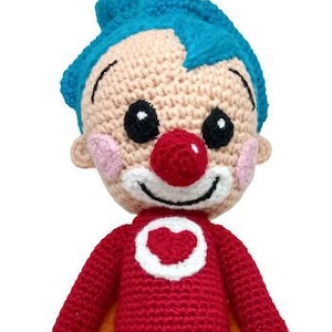 Pu&ograve; includere: Bambola pagliaccio all'uncinetto fatta a mano. La bambola ha un viso beige con capelli blu, un naso rosso e un sorriso bianco. Indossa un completo rosso con un cuore bianco e scarpe nere.