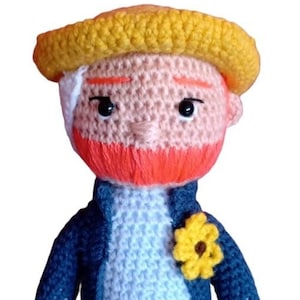 Può includere: Bambola all'uncinetto raffigurante una figura con cappello giallo, barba arancione e giacca blu. La bambola ha un fiore giallo sulla giacca e pantaloni beige. Gli occhi sono neri.