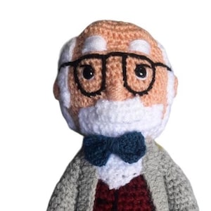 May include: Crocheted doll of a man with glasses, a white beard, and a bow tie. He wears a grey jacket over a burgundy vest and grey trousers. A small tag reads "El Yo y El Ello Freud."