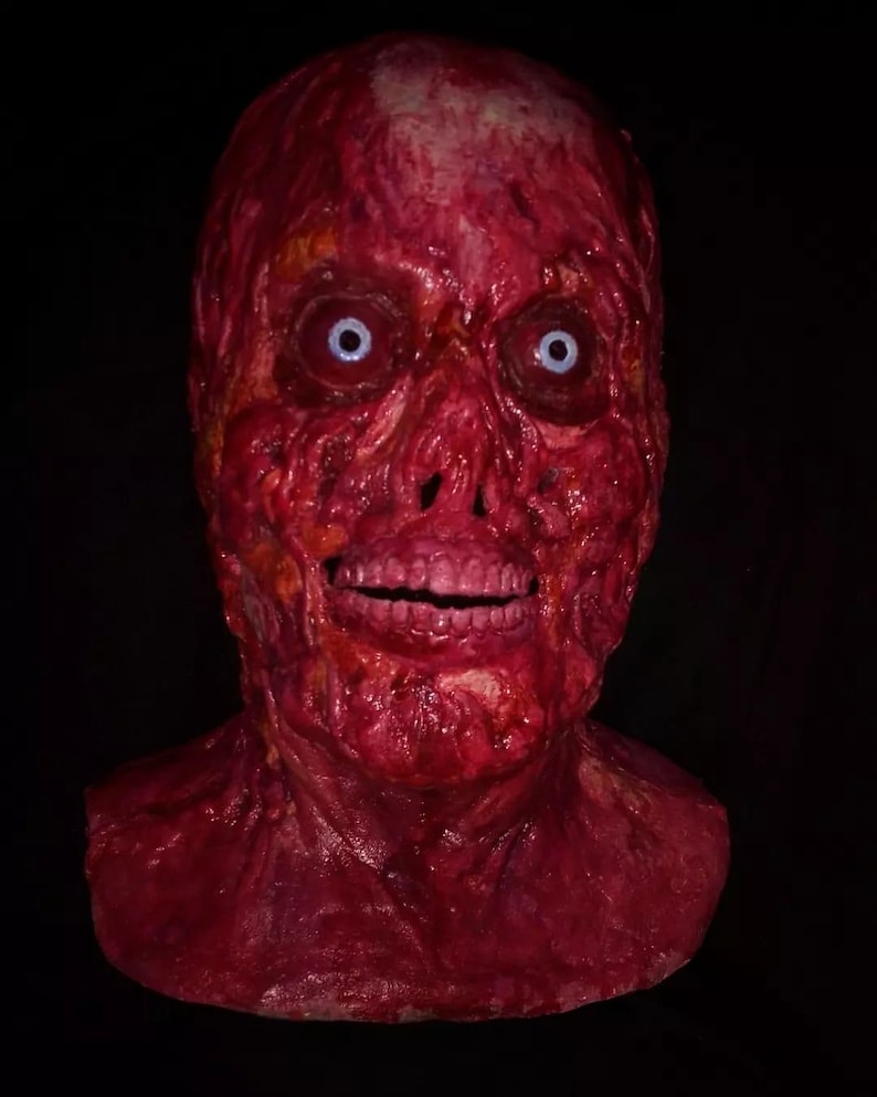 Pu&ograve; includere: Una spaventosa maschera di Halloween, in tonalit&agrave; rosse, raffigurante un volto in decomposizione con un sorriso sinistro. La maschera ha occhi azzurro pallido e una superficie strutturata e dettagliata. Progettata per essere indossata, copre il viso e il collo.